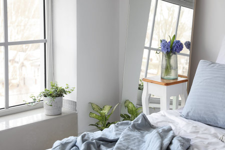 Vase with hyacinth flowers on table near mirror in light bedroom
