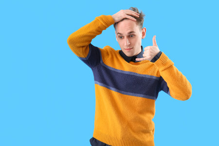 Young man showing call me gesture on blue background