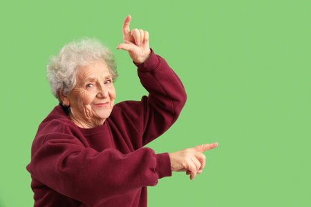 Senior woman showing loser gesture on green backgroundの写真素材