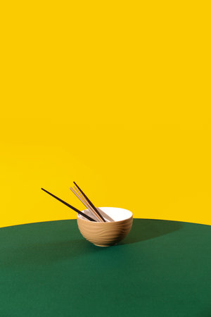 Bowl with chopsticks on table against yellow backgroundの写真素材