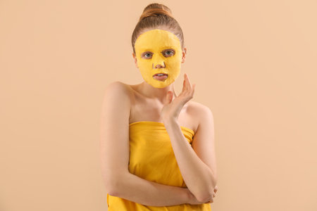 Young woman with turmeric sheet mask on beige backgroundの写真素材