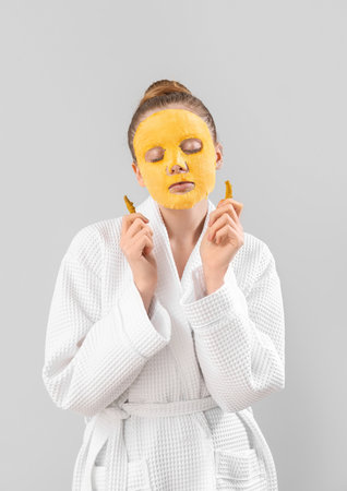 Young woman in bathrobe with turmeric sheet mask and roots on gray backgroundの写真素材
