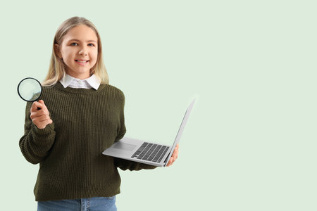 Little girl with magnifier and laptop on green backgroundの写真素材
