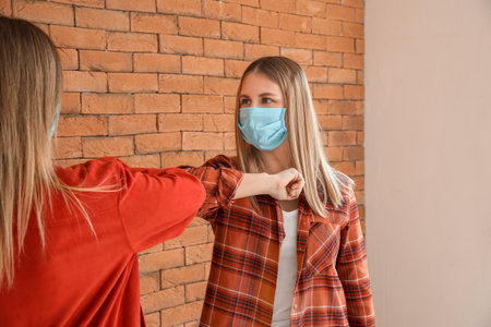 Young women greeting each other near brick wall. concept of social distance during coronavirus epidemicの写真素材