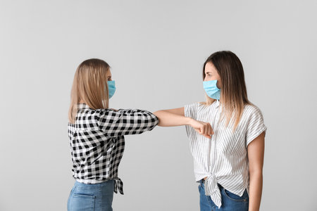 Young women greeting each other on light background. Concept of social distance during coronavirus epidemicの写真素材