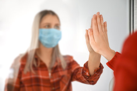 Women greeting each other through glass door. Concept of social distance during coronavirus epidemicの写真素材