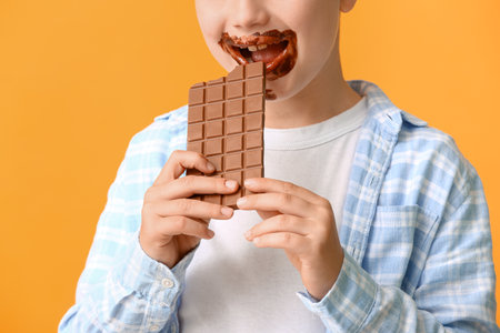 Cute little boy eating chocolate on color backgroundの写真素材
