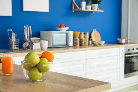 Bowl with fruits and glass of juice on table in modern kitchen