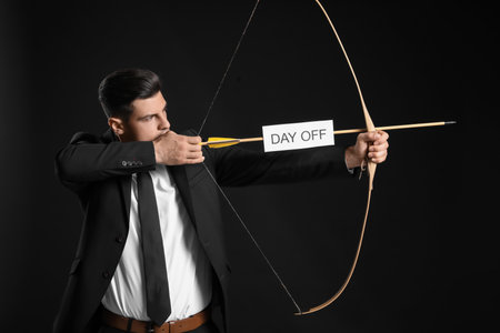 Businessman with crossbow and paper sheet with text DAY OFF on dark backgroundの写真素材