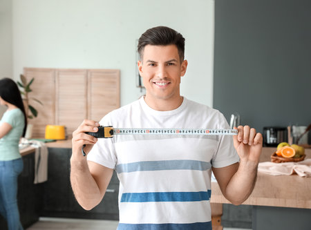 Young man with measuring tape in the kitchenの写真素材