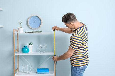 Young man taking measures of rack in roomの写真素材