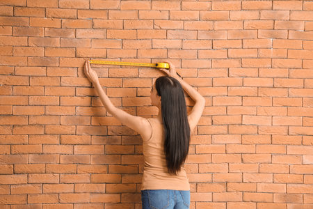 Young woman with measuring tape near brick wallの写真素材