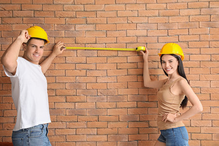 Couple with measuring tape near brick wall