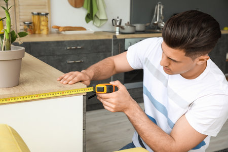 Young man taking measures of table in kitchenの写真素材