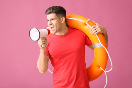 Beach rescuer with lifebuoy and megaphone on color backgroundの写真素材