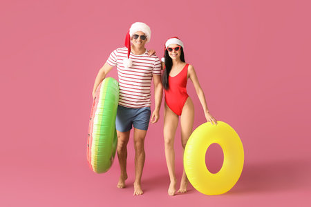Young couple with inflatable rings and Santa hats on color backgroundの写真素材