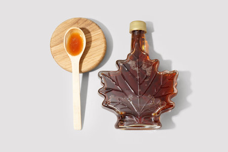 Bottle and spoon of tasty maple syrup on gray backgroundの写真素材