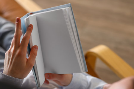 Young man reading book in armchair at home, closeupの写真素材