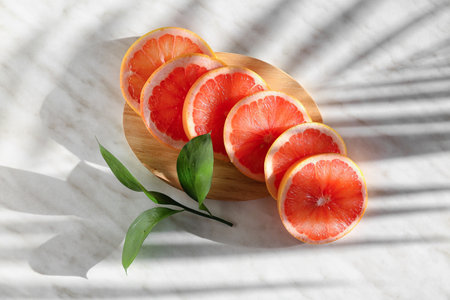 Wooden board with slices of ripe grapefruit and plant branch on light backgroundの写真素材