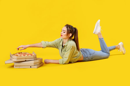 Young woman with cardboard boxes of tasty pizza lying on yellow backgroundの写真素材