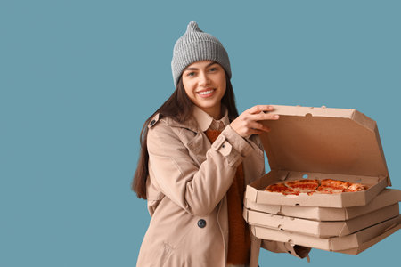 Young woman in hat with boxes of tasty pizza on blue backgroundの写真素材