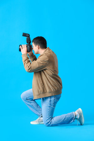 Young male photographer with professional camera on blue backgroundの写真素材