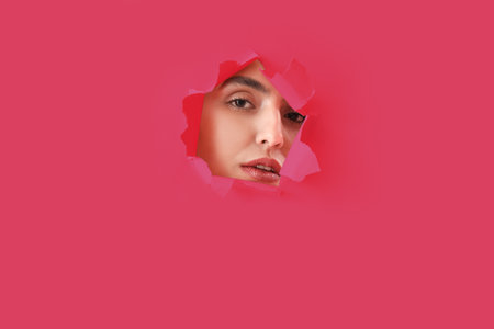 Young woman visible through hole in pink paperの写真素材