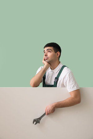 Thoughtful young plumber with wrench and blank poster on green backgroundの写真素材