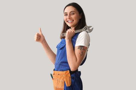 Female plumber with wrench showing thumb-up on gray backgroundの写真素材