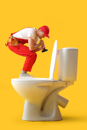 Young plumber with plunger and toilet bowl on yellow backgroundの写真素材