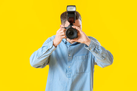 Male photographer with professional camera on yellow backgroundの写真素材