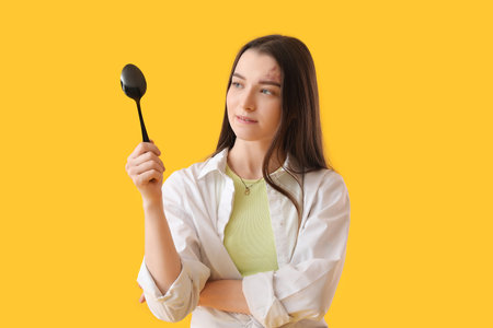 Young woman with black spoon on yellow backgroundの写真素材