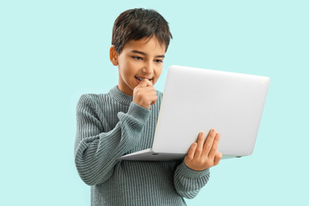Little boy with laptop biting nails on blue backgroundの写真素材