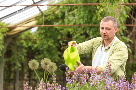 Male gardener with watering can in greenhouse