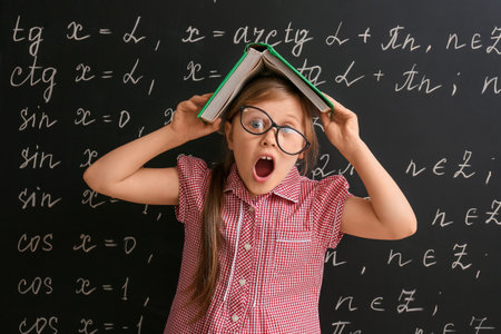 Funny little schoolgirl with book near blackboard in classroomの写真素材
