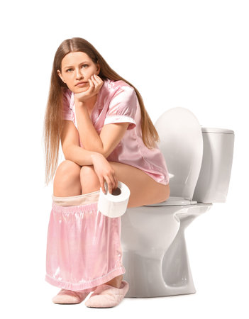 Young woman sitting on toilet bowl against white backgroundの写真素材