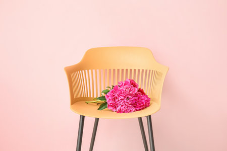 Beautiful peony flowers on chair against color backgroundの写真素材