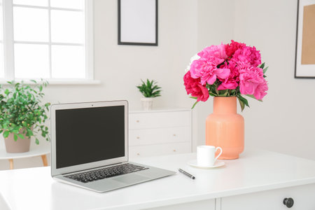 Vase with beautiful peony flowers and laptop on table in roomの写真素材