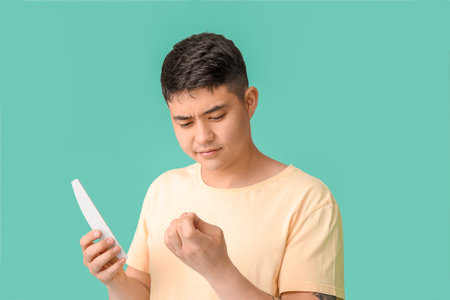 Asian man doing manicure on color backgroundの写真素材