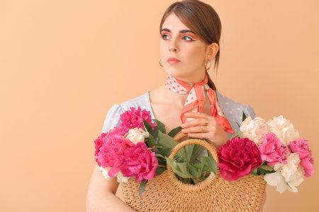 Young woman with beautiful peony flowers in bag on color backgroundの写真素材