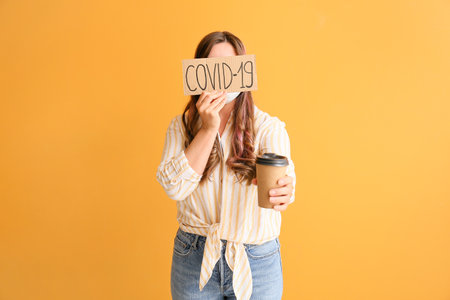 Young woman with cup of coffee on color background. concept of coronavirus epidemicの写真素材