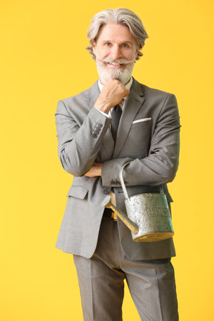 Senior businessman with watering can on color backgroundの写真素材