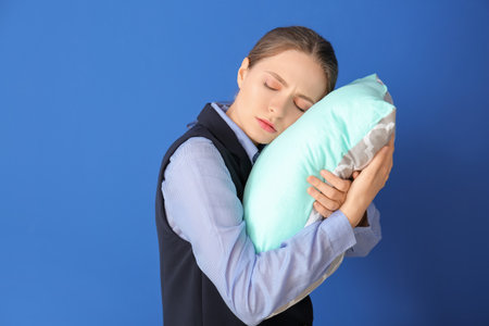 Tired woman with pillow on color background. Concept of sleep deprivationの写真素材