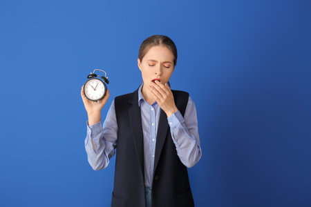 Tired woman with alarm clock on color background. Concept of sleep deprivation