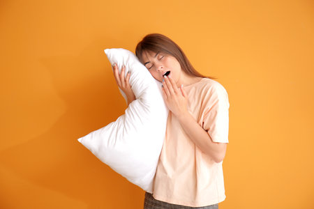 Tired woman with pillow on color background. Concept of sleep deprivationの写真素材