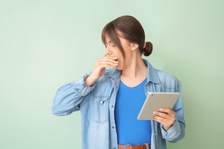 Tired woman with tablet computer on color background. Concept of sleep deprivationの写真素材