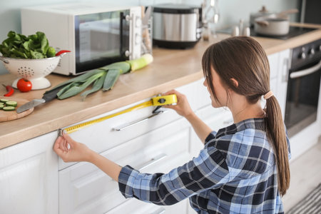 young woman measuring furniture in kitchenの写真素材