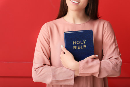 Young woman with Bible on color backgroundの写真素材
