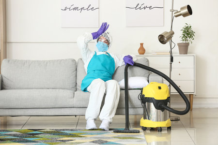 Tired housewife in protective costume during cleanup in roomの写真素材