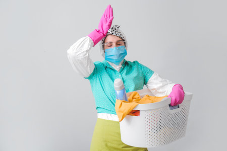 Tired housewife in protective costume and laundry on gray backgroundの写真素材